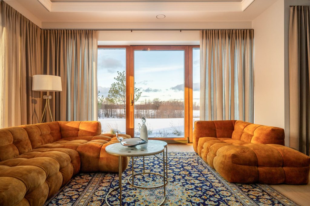 Neutralios spalvos užuolaidos interjere su ryškiai oranžiniu minkštasuoliu